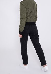 Olive green bomber jacket z prążkowanymi mankietami; czarne dżinsy; białe trampki. Gładka tekstura, dopasowany krój, widoczne detale szwów.