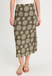 Jupe midi vert olive avec motif floral blanc, fabriquée en tissu léger. Elle présente une coupe droite et une fente sur le côté pour plus de liberté de mouvement.