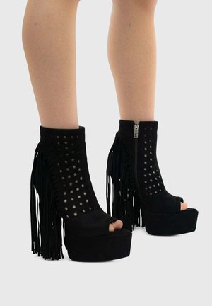 Stivaletti con plateau in camoscio nero, punta aperta, lati traforati, chiusure lampo e dettagli con frange lunghe sui tacchi.
