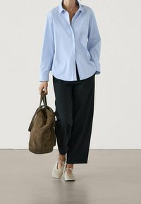 Light blue button-up shirt, black wide-leg pants, cream shoes with ties, and a brown suede tote bag. Smooth textures and casual design.