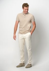 Beige kortärmad polo med krage och knapppdetail, kombinerad med vita byxor och ljusbeige sneakers. Släta texturer genom hela klädseln.