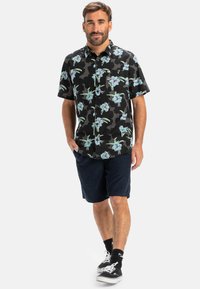 Cămașă neagră cu mâneci scurte, cu un model floral în nuanțe de albastru și verde, asociată cu pantaloni scurți închisi. Design casual, material ușor.