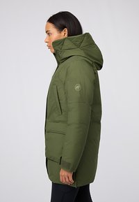 Parka verde con cappuccio, caratterizzata da un design trapuntato, tasche laterali e una toppa con logo sulla manica. Tessuto liscio e isolato.