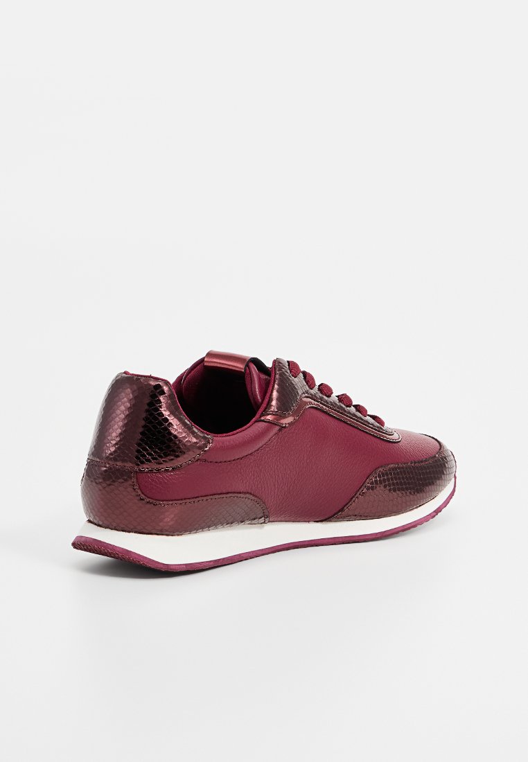 Sneaker borgogna con tacchi e punte metalliche testurizzati, allacciatura frontale e suola bianca, mostrato da vista posteriore su sfondo semplice.