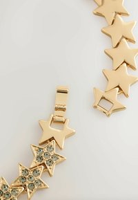 Kuldne tähekujuline käevõru, millel on siledad tähekujulised lingid ja üks, mis on kaunistatud selgete kristallidega. Sulgemismehhanism on nähtav, võimaldades kindlat kinnitamist.