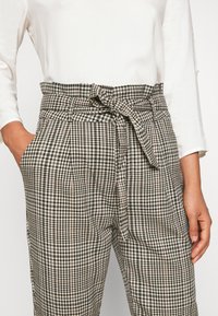 Rutig byxa med svart och vitt mönster, hög midja med tygbälte och sidofickor. Gjord av lättviktsmaterial.