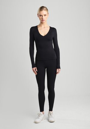 Musta pitkähihaine paita syvällä V-muotoisella kaula-aukolla, yhdistettynä mustiin legginsseihin. Molemmat ovat joustavaa materiaalia, tarjoten tiukasti istuvan siluetin.