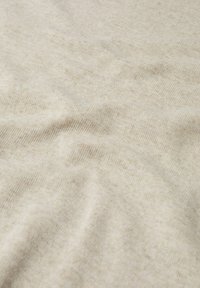 Tissu tricoté doux beige avec une texture subtile et des plis légers sous lumière naturelle.