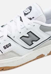 Fehér és szürke New Balance 550 sneaker perforált bőrrel, fehér fűzőkkel és ragasztott talppal, oldalán a logóval és a modell számmal.