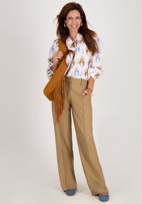 Witte blouse met blauw en bruin patroon, tan wijde broek, bruine franjes tas en lichtblauwe schoenen. Eenvoudige sieraden als accenten.