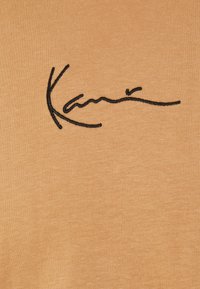 Tela de color naranja claro con una textura suave que presenta un diseño de firma bordado en negro. La tela es suave y elástica.