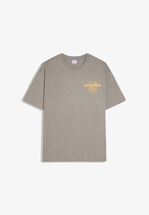 Tričko farby taupe s krátkym rukávom a okrúhlym výstrihom s žltým textom na hrudi: „Príliš zaneprázdnený byť bezstarostný na to, aby som zdvíhal tvoje hovory.”