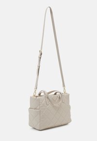 Vadderad beige handväska med dubbla handtag och en avtagbar axelrem. Har en strukturerad form och en sidoficka för förvaring.