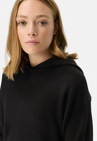 Zwarte hoodie gemaakt van gestructureerde stof. Heeft een relaxte pasvorm en een eenvoudig ontwerp zonder zichtbare logo's of patronen.