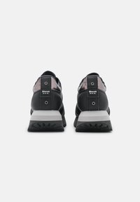 Ett par svarta och grå Blauer U.S.A. sneakers visade bakifrån, med fokus på tjocka sulor och metalliska detaljer nära hälen.