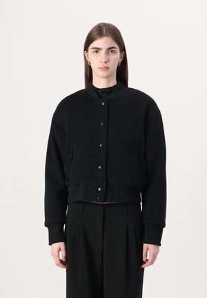 Svart cropped bomberjakke med trykknapper, ribbestrikkede ermer og sidelommer. Laget av et mykt stoff med en glatt tekstur.