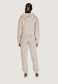Felpa cropped beige chiaro con pantaloni joggers coordinati, caratterizzata da un taglio rilassato, polsini a costine e vita elasticizzata. Tessuto testurizzato.