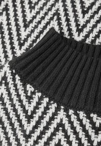 Maglione lavorato a maglia con motivo a zigzag bianco e nero e collo a coste nero per aggiungere texture e contrasto.
