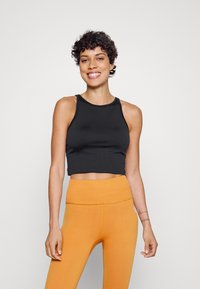 Top cropped preto com decote redondo, combinado com leggings laranjas caneladas de cintura alta. Tecido suave com costuras mínimas.