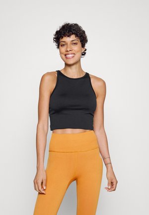 Top cropped preto com decote redondo, combinado com leggings laranjas caneladas de cintura alta. Tecido suave com costuras mínimas.
