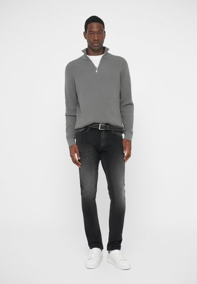 Gray zippered sweater with ribbed texture, paired with dark jeans and white sneakers. The outfit features a classic fit and subtle contrasts.