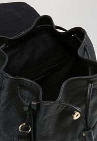 Sac seau en cuir noir avec fermeture à cordon, garnitures dorées et un intérieur spacieux doublé de tissu noir.
