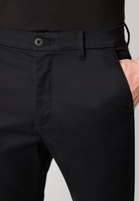 Zwarte pantalons van gladde stof met een platte voorkant, zijzakken en riemlussen, voorzien van een knoopsluiting en een subtiele textuur.
