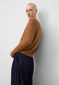 Maglione in misto mohair marrone con vestibilità comoda e maniche lunghe, abbinato a pantaloni di jeans scuri con tasche laterali e cuciture a vista.