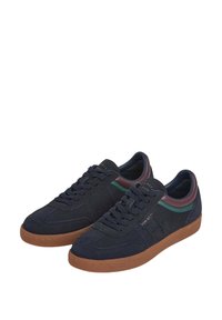 Par de zapatillas de ante azul marino con suelas de goma marrón, Accentos de cuero verde y marrón, cordones negros y nombre de la marca en el lateral.