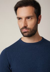 Granatowy męski sweter z dzianiny o okrągłym dekolcie, wykonany z miękkiego materiału, o dopasowanym kroju i prążkowanym wykończeniu przy szyi. Bez widocznych wzorów czy ozdób.