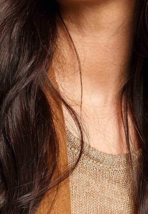 Cheveux longs et foncés tombant sur un pull en tricot beige et un col de manteau marron, mettant en valeur le cou et la partie supérieure de la poitrine.