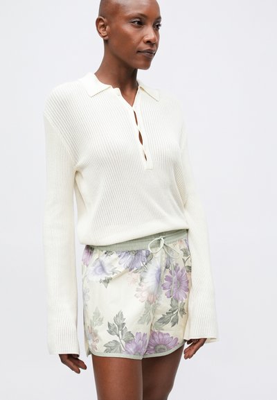 Polo de manga larga de punto acanalado en color blanco roto combinado con pantalones cortos florales claros que cuentan con un cordón y acentos verdes.