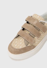 Sneaker beige con tre strappi in velcro, tomaia testurizzata e punta in suede. Presenta un design a pattern sottile e una suola bianca.