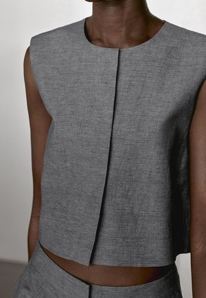 Haut court gris texturé sans manches avec une couture centrale à l’avant, porté par une personne à la peau foncée.