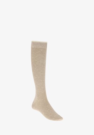 Chaussette beige montant jusqu'au genou avec de petits pois blancs, présentée à la verticale sur un fond blanc.