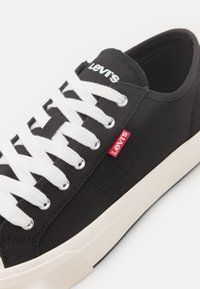 Černé plátěné tenisky s bílými šňůrkami, s červeným logem Levi's, stříbrnými oky a bílou strukturovanou gumovou podrážkou.