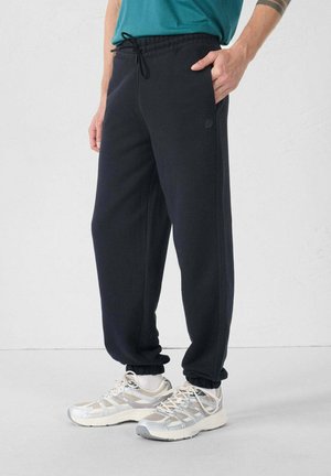 Navy joggingbroek met een trekkoord in de taille, elastische boorden, zijzakken en een klein logo op de dij, gecombineerd met lichte sneakers.