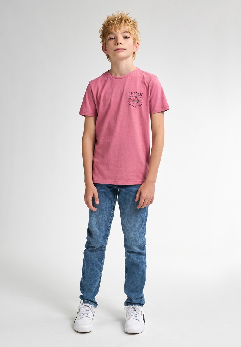 Lyserød bomulds t-shirt med korte ærmer og et sort grafisk logo på brystet, parret med blå denim jeans og hvide sneakers.