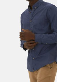 Camisa de botones azul marino con cuello, un bolsillo en el pecho y mangas con puños abotonados. Tejido de algodón suave con un diseño ajustado.