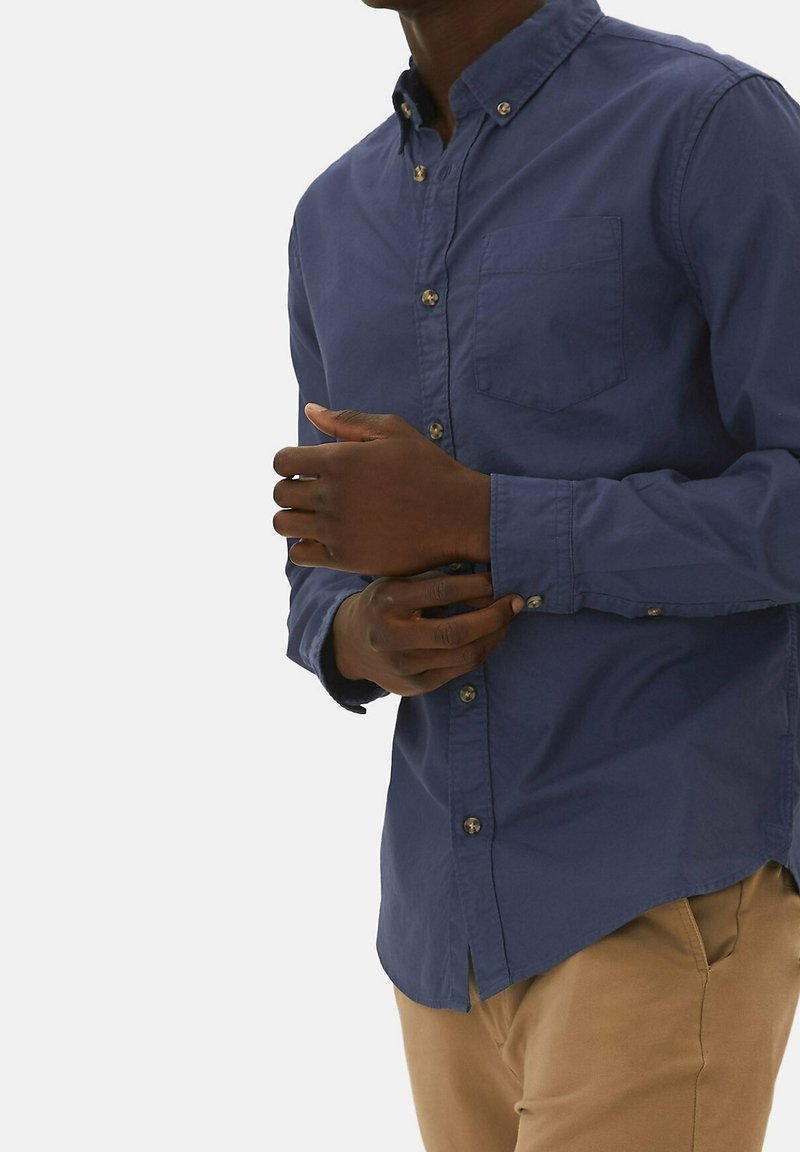 Camisa de botones azul marino con cuello, un bolsillo en el pecho y mangas con puños abotonados. Tejido de algodón suave con un diseño ajustado.
