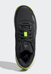 Chaussure de sport noire avec tige en mesh, accents verts et logo réfléchissant. Comprend un col rembourré et des lacets plats pour un ajustement sécurisé.