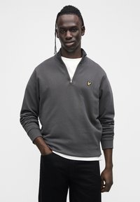 Gray zip-up sweatshirt with long sleeves, featuring a white undershirt and a small gold logo on the chest. Soft fabric texture.