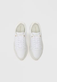 Bílé tenisky s hladkým koženým svrškem, zlatými detaily na očkách a polstrovanou, světlou podrážkou. Jednoduchý design s tkaničkami.