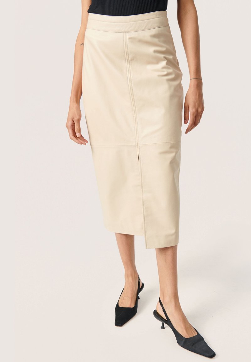 Cremfarbene Midi-Rock aus Leder mit tailliertem Bund, seitlichem Schlitz und Nahtdetails. Kombiniert mit schwarzen Slingback-High Heels. Glatte Textur.