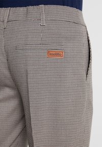 Checked trousers in black and white fabric with a smooth texture. Features a brown leather logo patch on the back pocket.