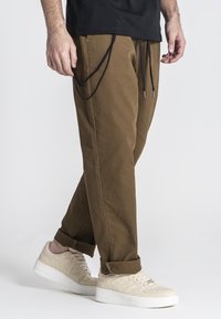 Bruine katoenen broeken met een ontspannen pasvorm, voorzien van zwarte trekkoorden en zijzakken, gecombineerd met beige sneakers. Eenvoudig ontwerp, zonder patronen.