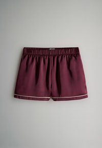 Bordó fürdőnadrág elasztikus derékpánttal, sima textúrával és kontrasztos fehér szegéllyel az alsó szélén. Zsebek nélküli.