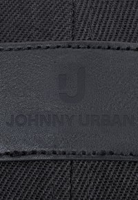 Petecă din piele neagră cu logo "Johnny Urban" în relief pe un fundal din material texturat negru cu cusături vizibile.