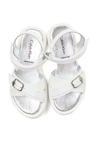 Białe sandały z błyszczącą srebrną wkładką, posiadające sprzączkę na pasku i miękką teksturę. Zaprojektowane z otwartym noskiem i regulowanym zapięciem na sprzączkę.