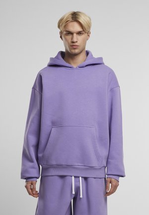 Sweatshirt à capuche violet en tissu doux, avec une poche avant et un ourlet côtelé. Associé à un pantalon de jogging assorti, avec des cordons blancs.
